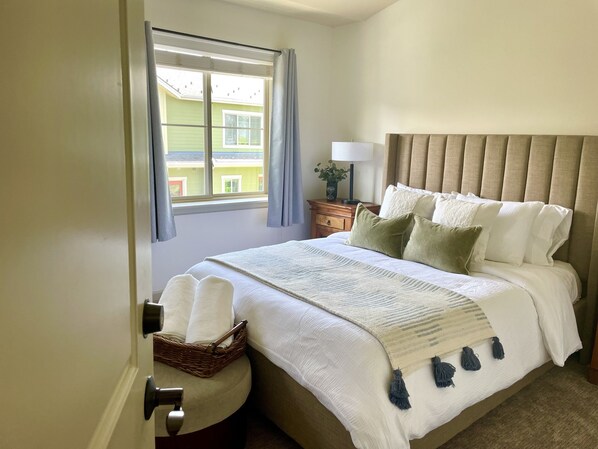 Une chambre bien rangée, avec un lit, une table de chevet, une lampe et une vue sur un bâtiment à l’extérieur.