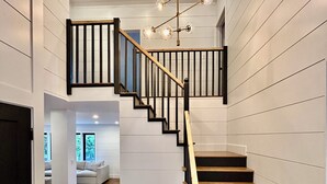 Un escalier moderne avec des marches en bois et des rampes noires, menant à un deuxième étage doté d’une lucarne.