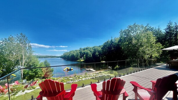 Une terrasse avec des chaises rouges donnant sur un lac, entourée de verdure.