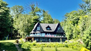 Une grande maison dotée d’un balcon donnant sur un lac, entourée d’une végétation luxuriante.