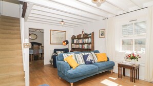 A living room with a blue sofa, wooden flooring, a bookshelf, and a staircase.