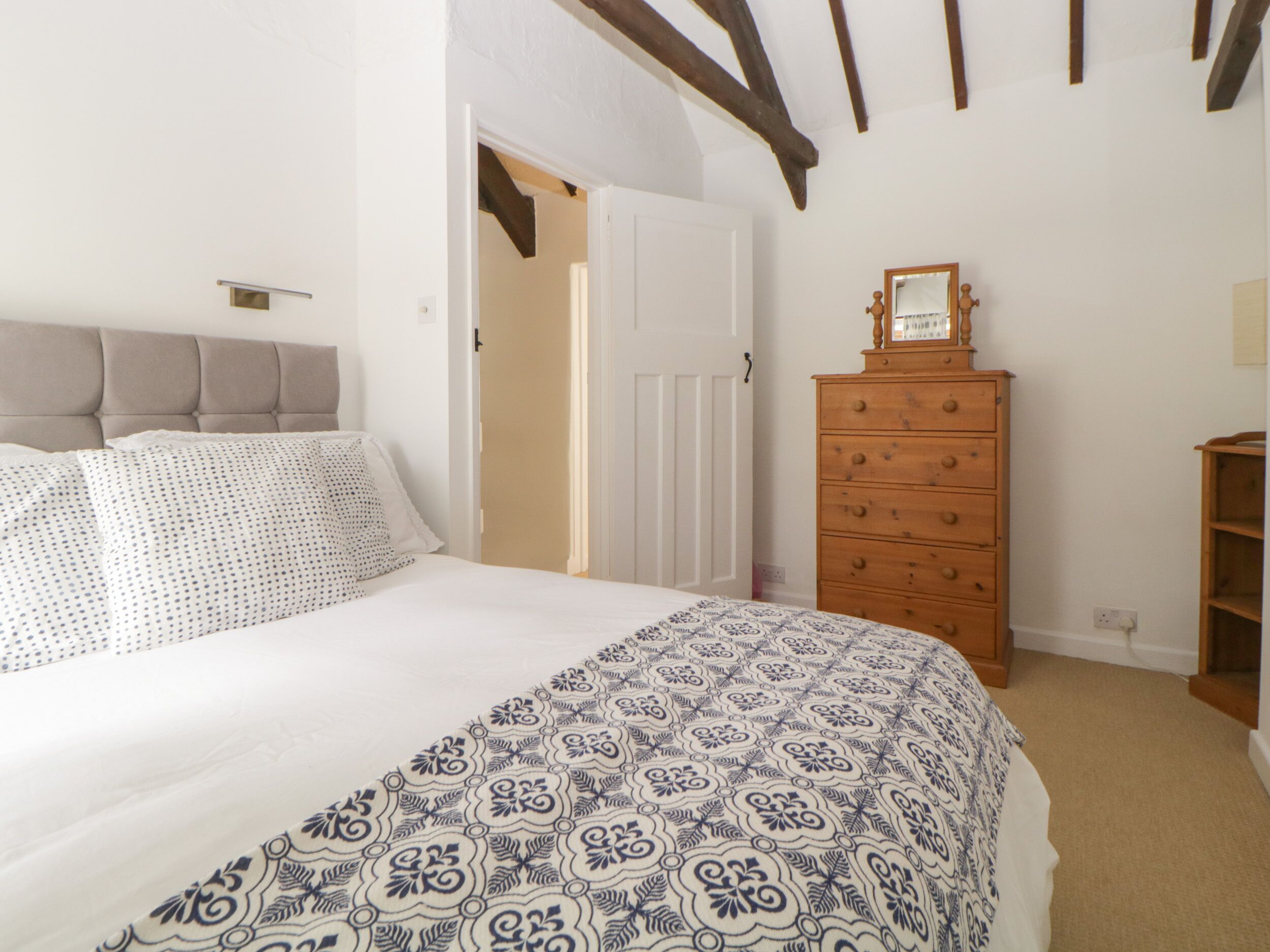 A bedroom with a bed, a dresser, and a door leading to another room.