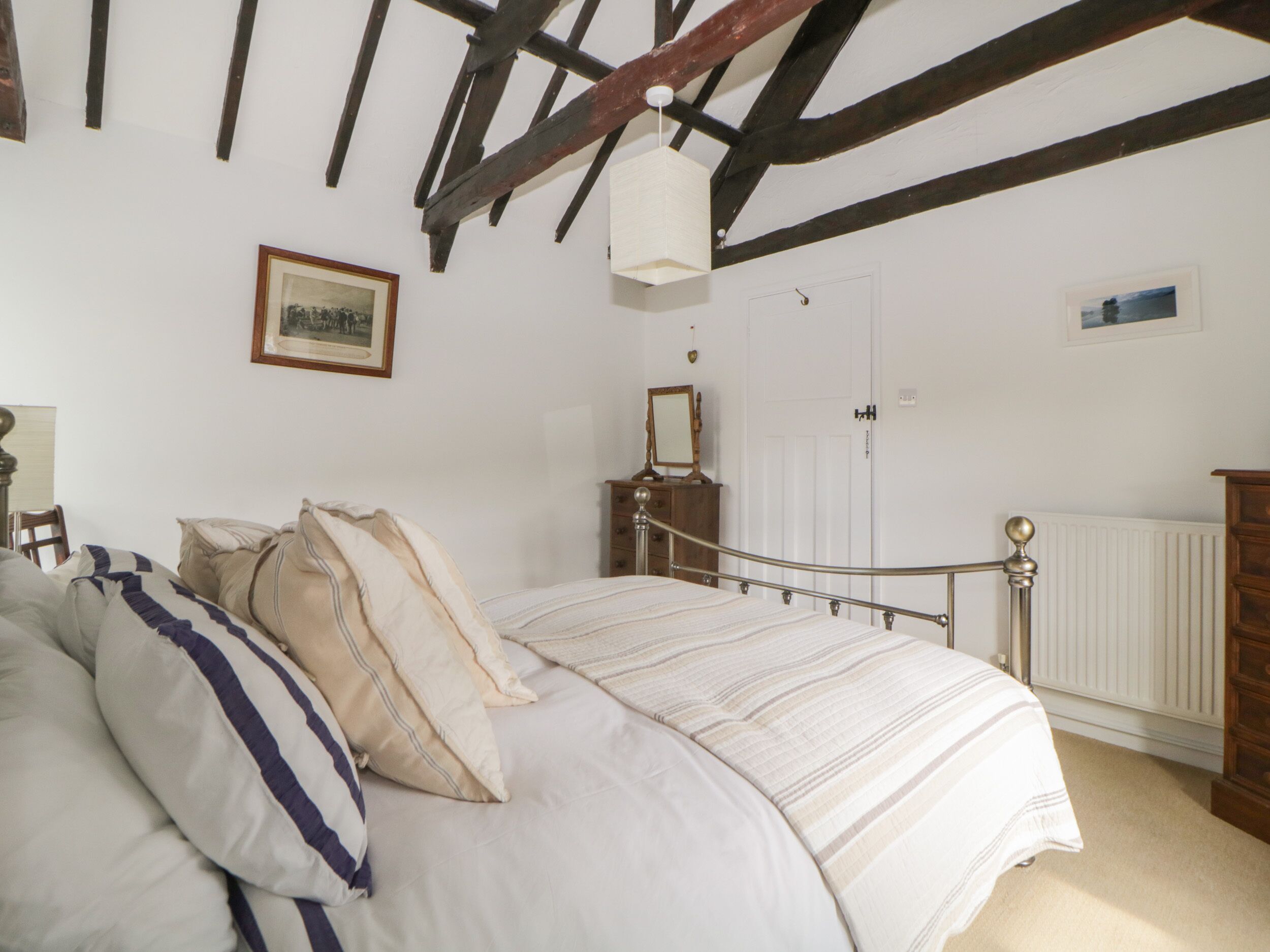 A bedroom with a bed, a dresser, a mirror, and a framed picture on the wall.
