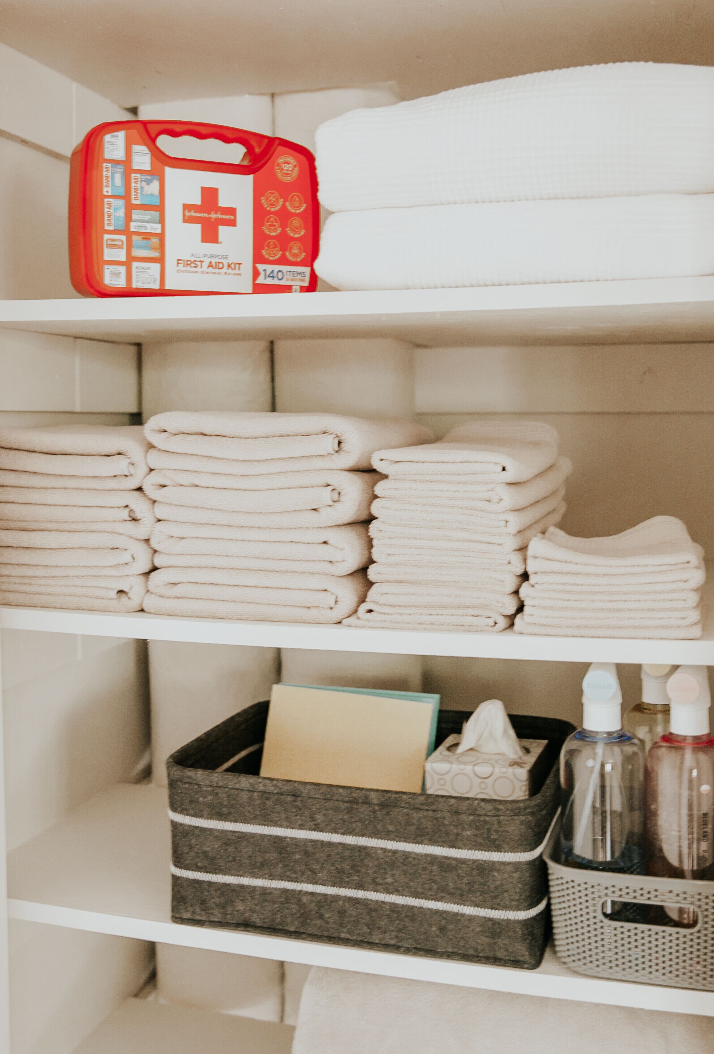 Une étagère dans la salle de bain contenant une trousse de premiers secours, des serviettes pliées et des articles de toilette.