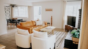 Una sala moderna con un sofá, dos sillones, una mesa de centro, un televisor y un comedor con una mesa y sillas.