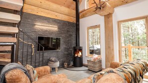 Un interior moderno con chimenea, escalera de madera y ventanas amplias.