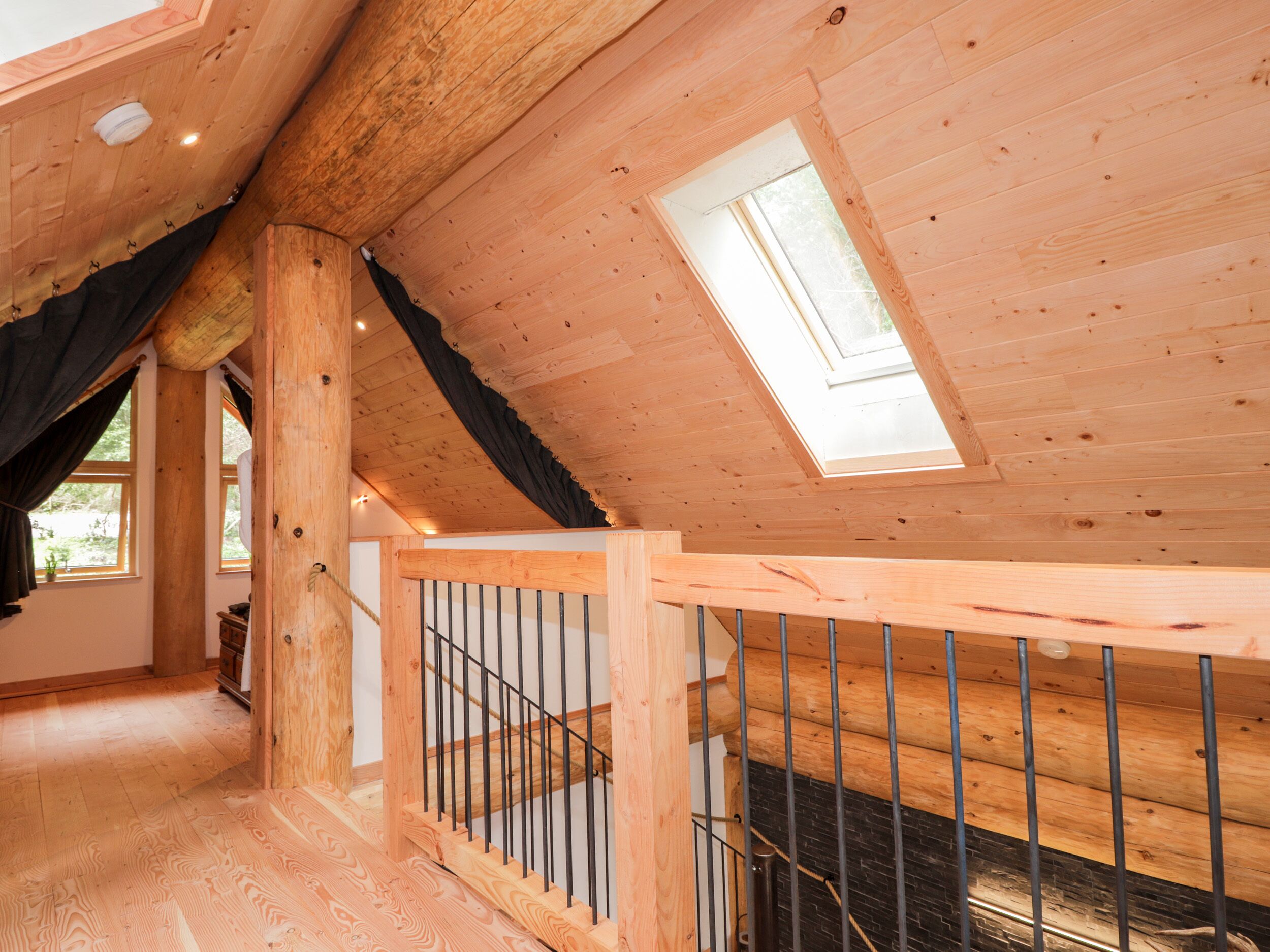 A wooden interior with a sloped ceiling, a skylight, and a staircase with a wooden railing.