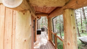 Una cabaña de madera con un porche cubierto, un ventilador y un banco.