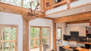 Amplia sala de estar con un ventanal grande, techo de madera y una cocina equipada con electrodomésticos modernos.