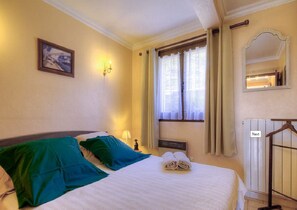 Une chambre d’hôtel avec un lit, une fenêtre avec des rideaux, un miroir fixé au mur et un radiateur.