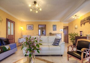 Un salon avec un canapé blanc, une chaise en bois, un vase de fleurs et un lustre.