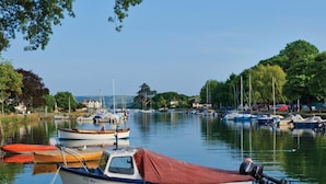 En lugn hamn med flera båtar förtöjda, omgiven av frodig grönska och en klar himmel.