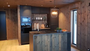 A modern kitchen with wooden paneling, a central island, and a hanging light fixture. - Luxury cabin: Modern and stylish (Torpo)