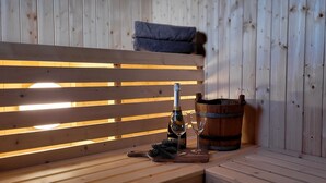 A wooden bench with a bottle and glass, a wooden bucket, and a cushion against a wooden wall. - Luxury cabin: Modern and stylish (Torpo)