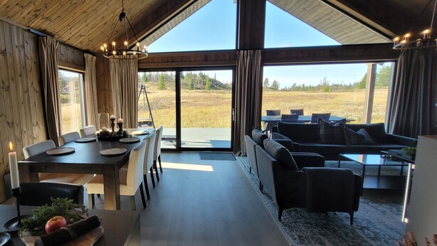 A spacious room with a large dining table set for four, a sofa, and a view of a natural landscape. - Luxury cabin: Modern and stylish (Torpo)