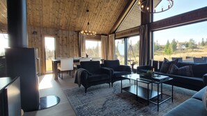 A cozy living room with a fireplace, comfortable seating, and large windows offering a view of the outdoors. - Luxury cabin: Modern and stylish (Torpo)