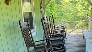 A porch with wooden rocking chairs and a bench, green wooden walls, and a view of trees. - Rustic Tennessee Farmhouse on 100 acres of land (Bethpage)