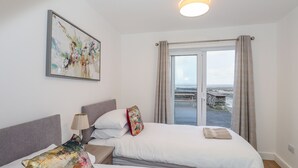 A bedroom with two beds, a painting, a lamp, and a view of the sea through a glass door. - The Lookout (Millom)