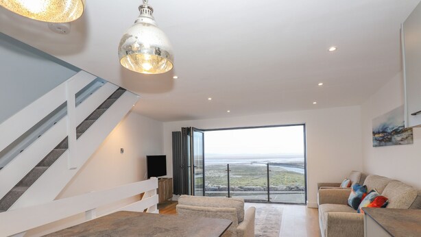 A modern living room with a large window, a staircase, and a dining area. - The Lookout (Millom)