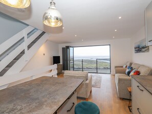 A modern living room with a large window, a staircase, and a dining area. - The Lookout (Millom)