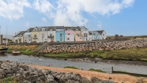 A row of colorful houses by a river with a stone wall in the foreground. - The Lookout (Millom)