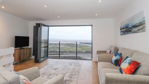 A modern living room with a large sliding glass door leading to a balcony with a view of the sea. - The Lookout (Millom)