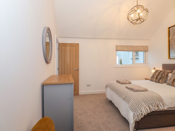 A bedroom with a bed, a bedside table, a mirror, a window, and a chandelier. - The Lookout (Millom)