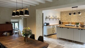 Una cocina moderna con una isla central, iluminación colgante y un comedor con mesa y sillas de madera.