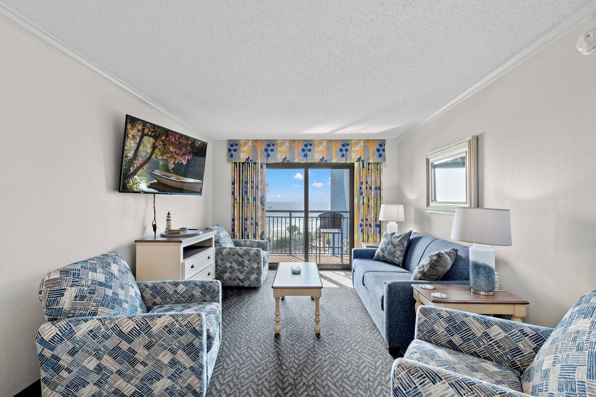 A hotel room with a balcony, a television, a sofa, a coffee table, and a lamp.