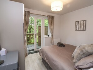 A bedroom with a bed, a bedside table, a window with curtains, and a view of greenery outside. - Treetops (Ottery St Mary)