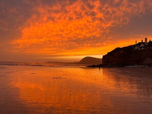 A beach at sunset with a cliff and houses in the background. - Treetops (Ottery St Mary)