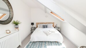 A modern bedroom with a sloped ceiling, a large bed with white bedding, a small plant, and a patterned rug.