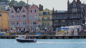 A waterfront with colorful buildings, a dock, and a boat named 'PILOT 4'.