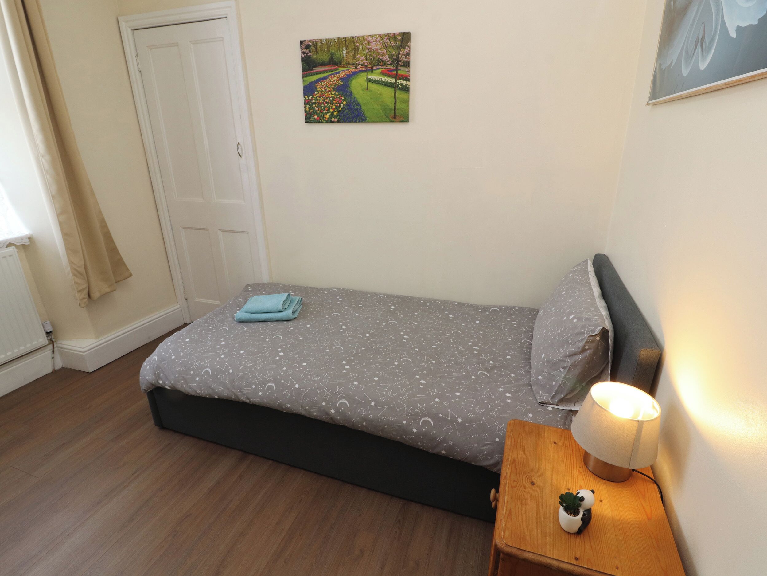 Une chambre à coucher avec un lit, une table de chevet avec une lampe, une petite plante en pot et un tableau accroché au mur.