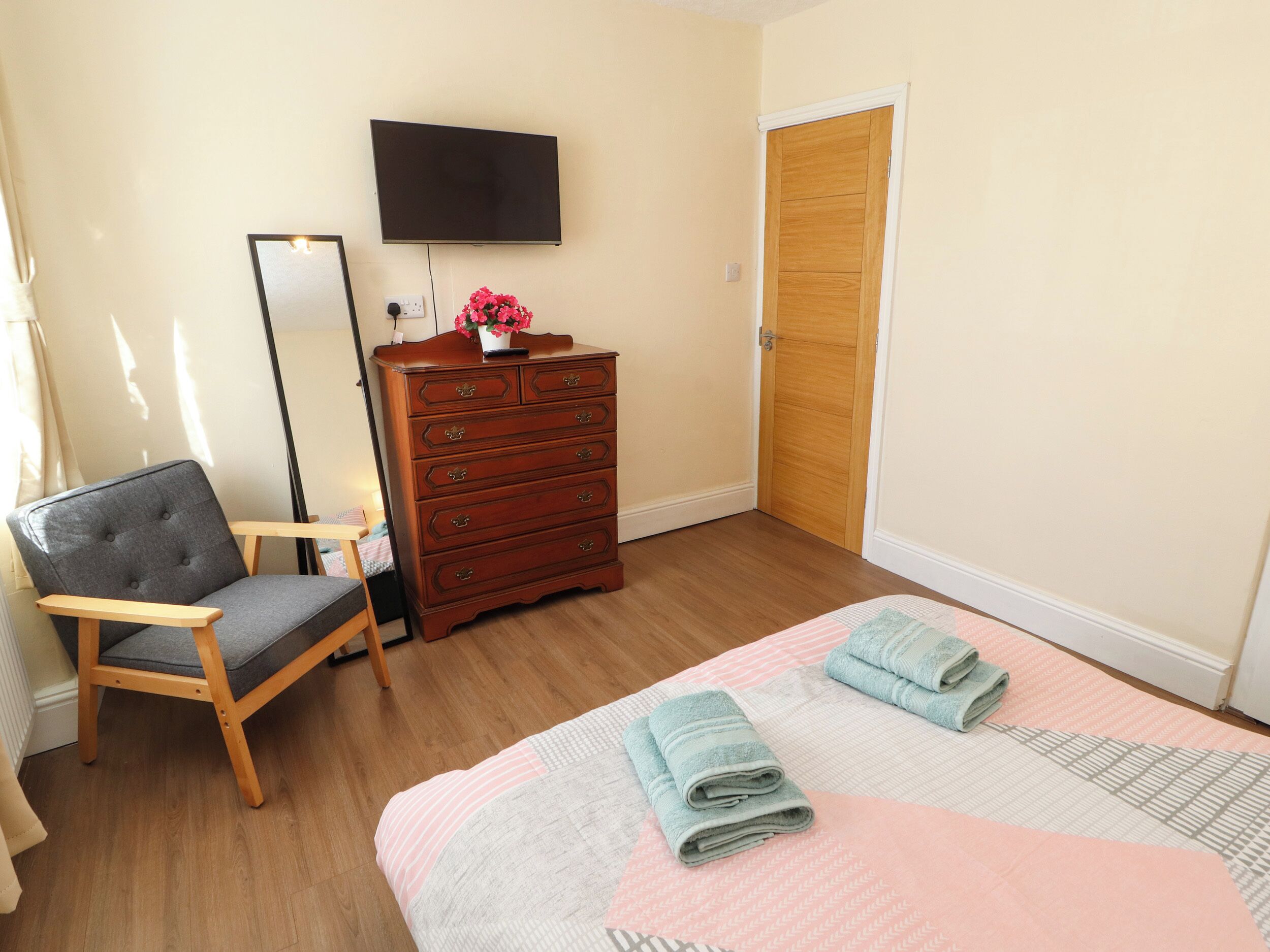 Une chambre à coucher avec un lit, une commode, une chaise, un téléviseur et une porte.