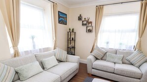 A living room with two sofas, a small side table, a bookshelf, and a window with curtains. - Neland View (Windermere)