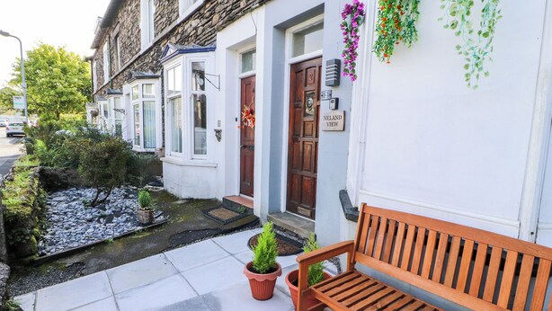 A row of white houses with stone facades, a wooden bench, and a small garden with potted plants. - Neland View (Windermere)