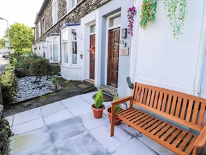 A row of white houses with stone facades, a wooden bench, and a small garden with potted plants. - Neland View (Windermere)