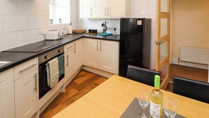 A modern kitchen with white cabinets, a black refrigerator, and a dining table with wine glasses. - Neland View (Windermere)