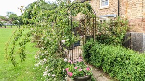A stone cottage with a garden featuring a metal arbor and flowering plants.