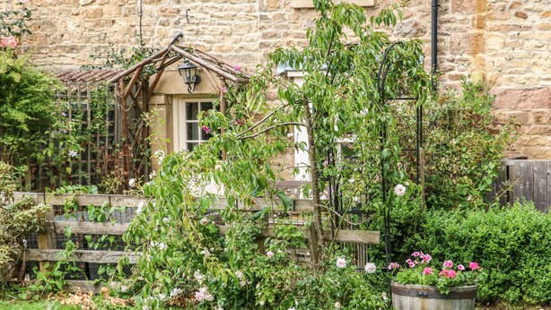 A stone building with a wooden fence, a wooden arbor, and a variety of flowering plants.