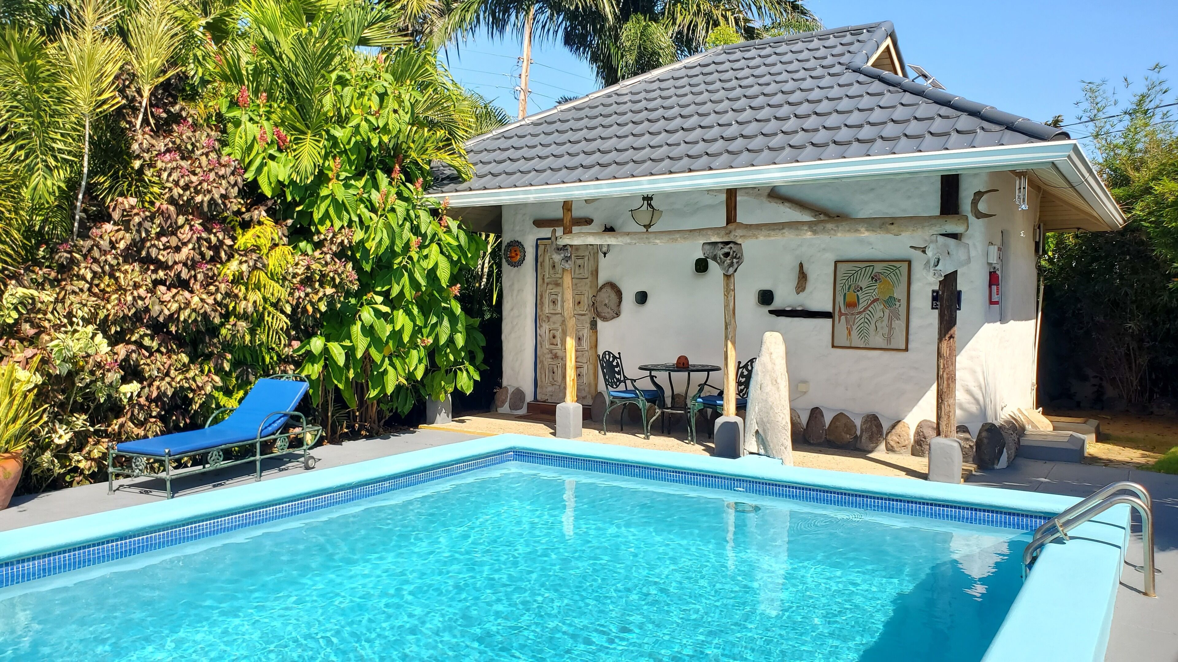 Una piscina con borda piastrellata, una poltrona da relax blu e un tavolo con sedie.