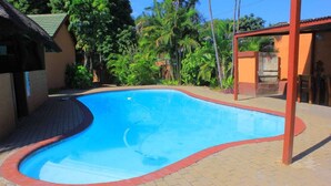 Piscina com borda curva, rodeada por um pátio de tijolos e um deck de madeira.