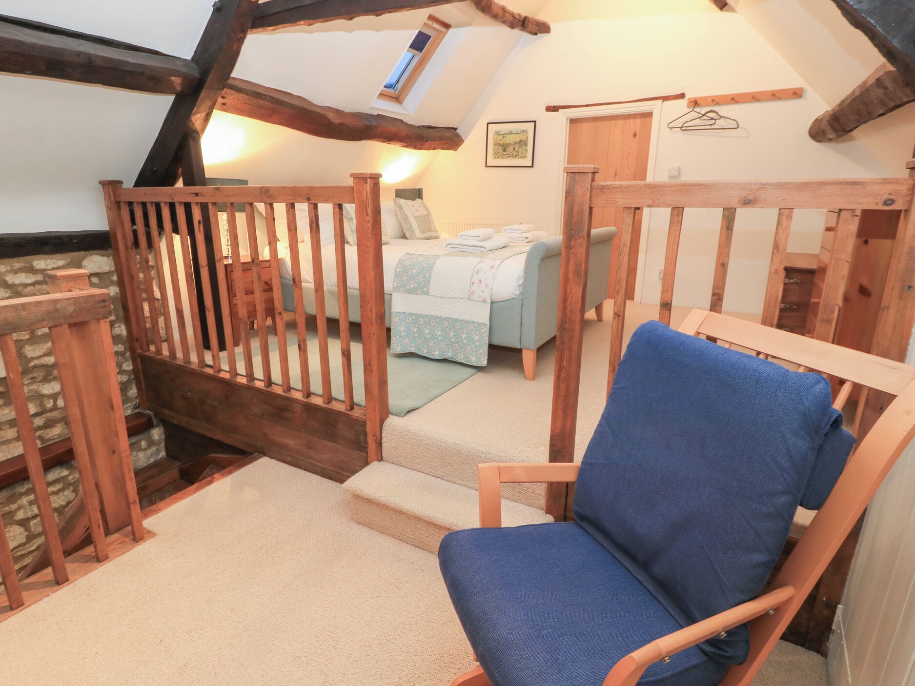 A cozy attic bedroom with a wooden staircase, a single bed, and a blue chair.