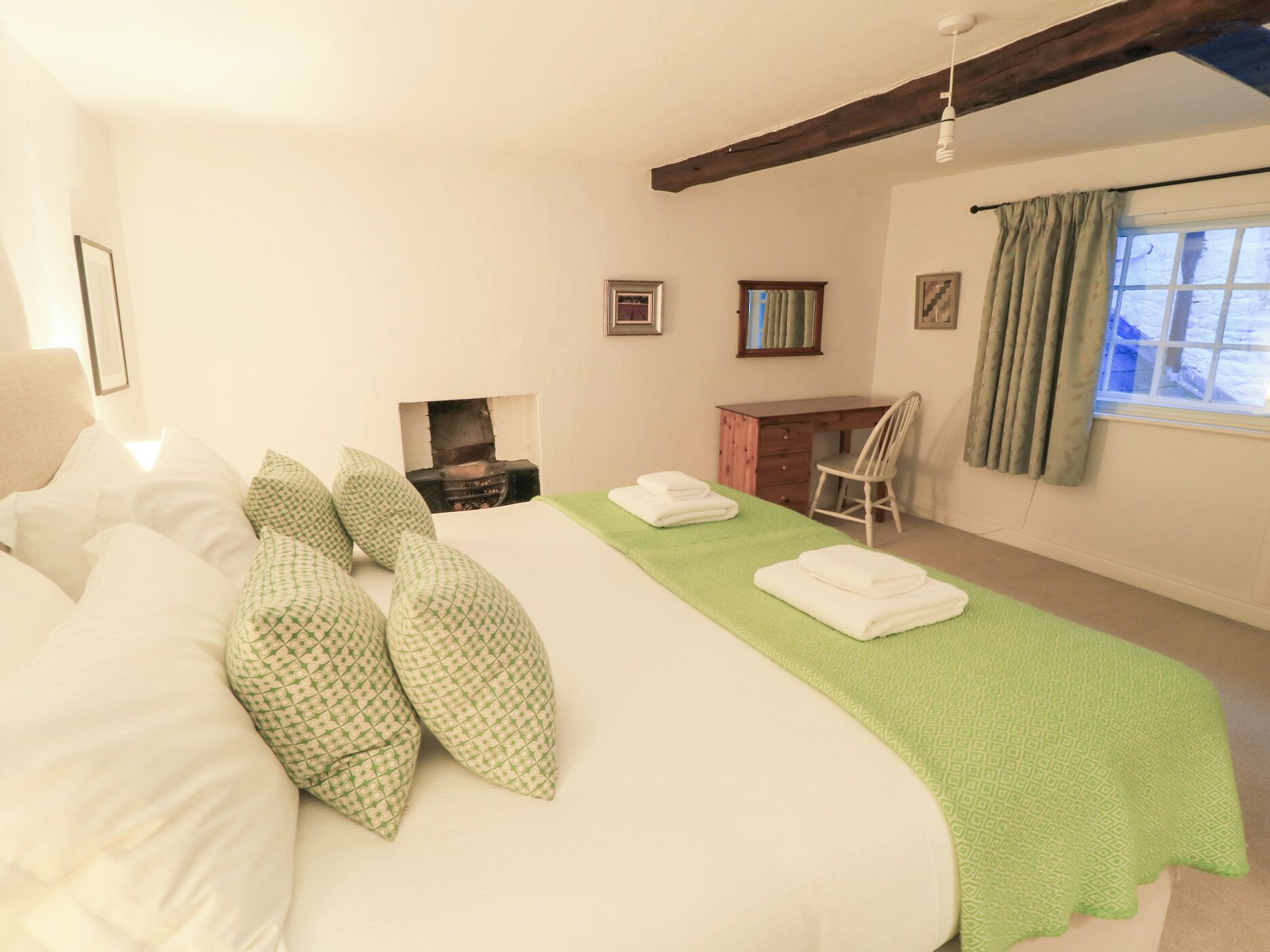 A bedroom with a large bed, a desk, a chair, and a fireplace.