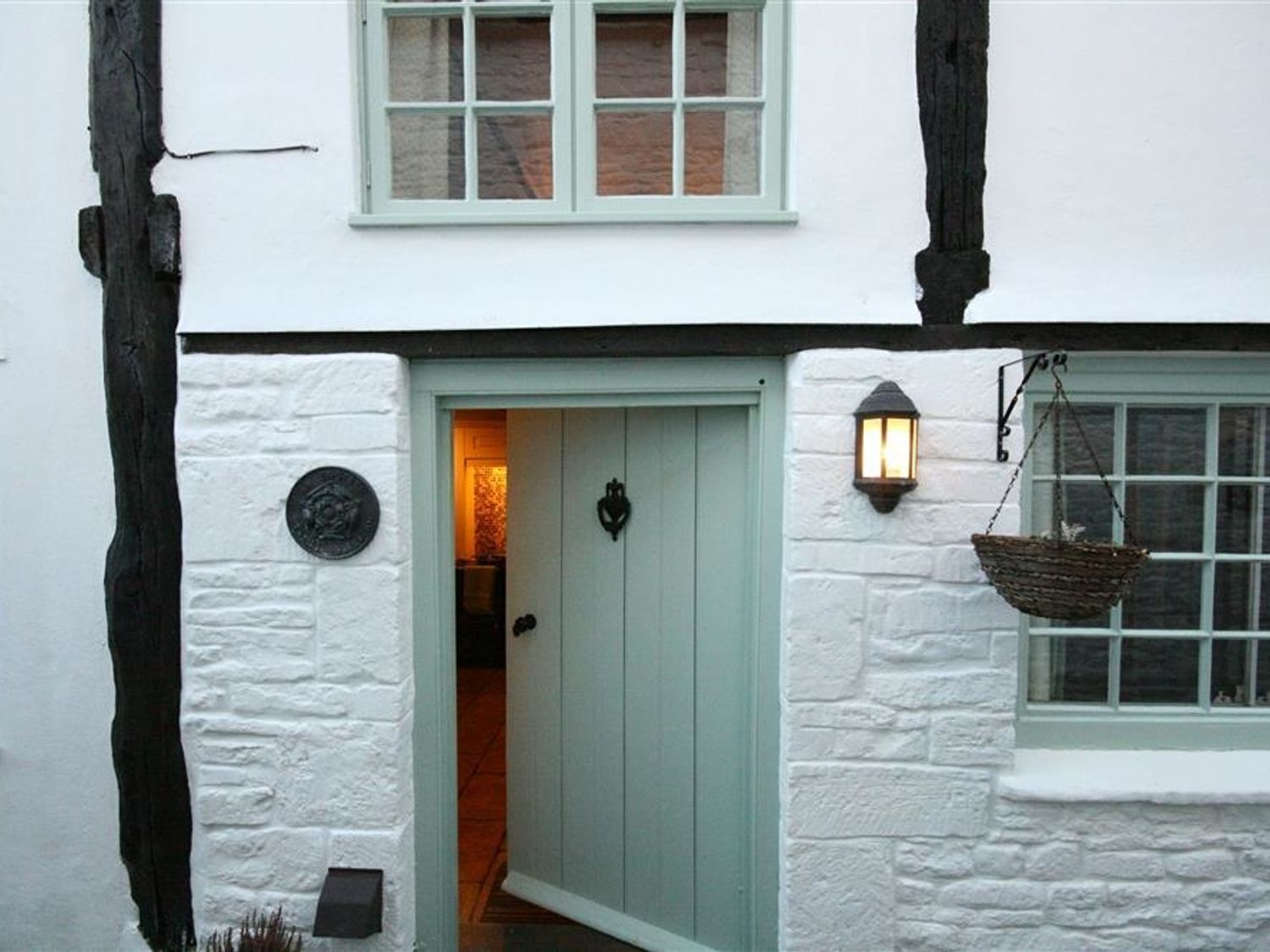 A traditional building with a light green door, a hanging basket, and a stone wall.
