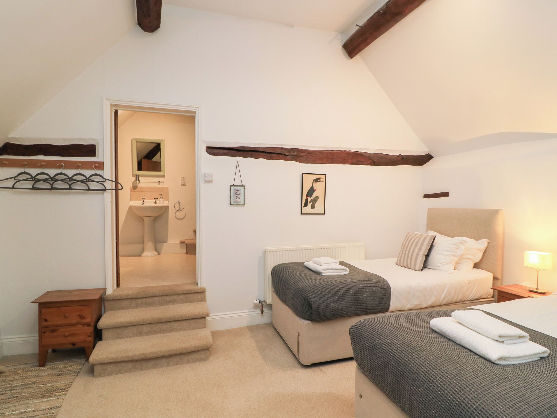 Een slaapkamer met een bed, nachtkastje en een klein nachtkastje. Er is een trap naar een aangrenzende badkamer.