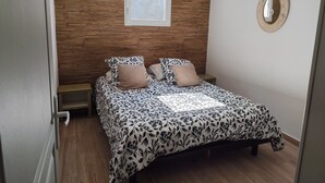A bedroom with a wooden headboard, a bed with floral bedding, a bedside table, and a hanging light fixture. - Appart-hôtel-piscine (Fréjus)