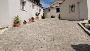 A courtyard with potted plants and a paved walkway leading to a building with multiple windows. - Appart-hôtel-piscine (Fréjus)