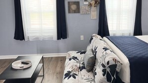 A modern bedroom with a bed, a ceiling fan, a wall-mounted air conditioner, and a window with sheer curtains. - The Mark at Surfside, Apt. 5 (Surfside Beach)